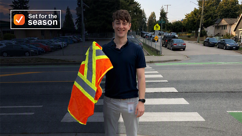 Dr. Curtis May, medical health officer, holding up a high-visibility vest, standing at a crosswalk. 
