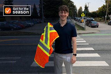 Dr. Curtis May, medical health officer, holding up a high-visibility vest, standing at a crosswalk. 