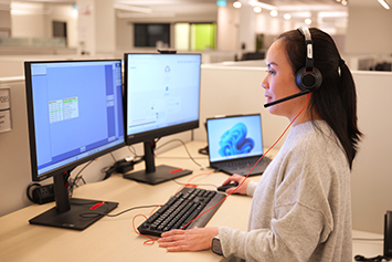 Registered nurse wearing a headset sitting at a desk in front of computer screens