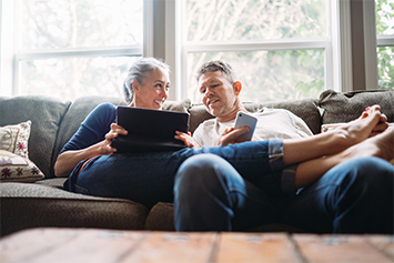 Older couple relaxing on a couch looking a tablet device